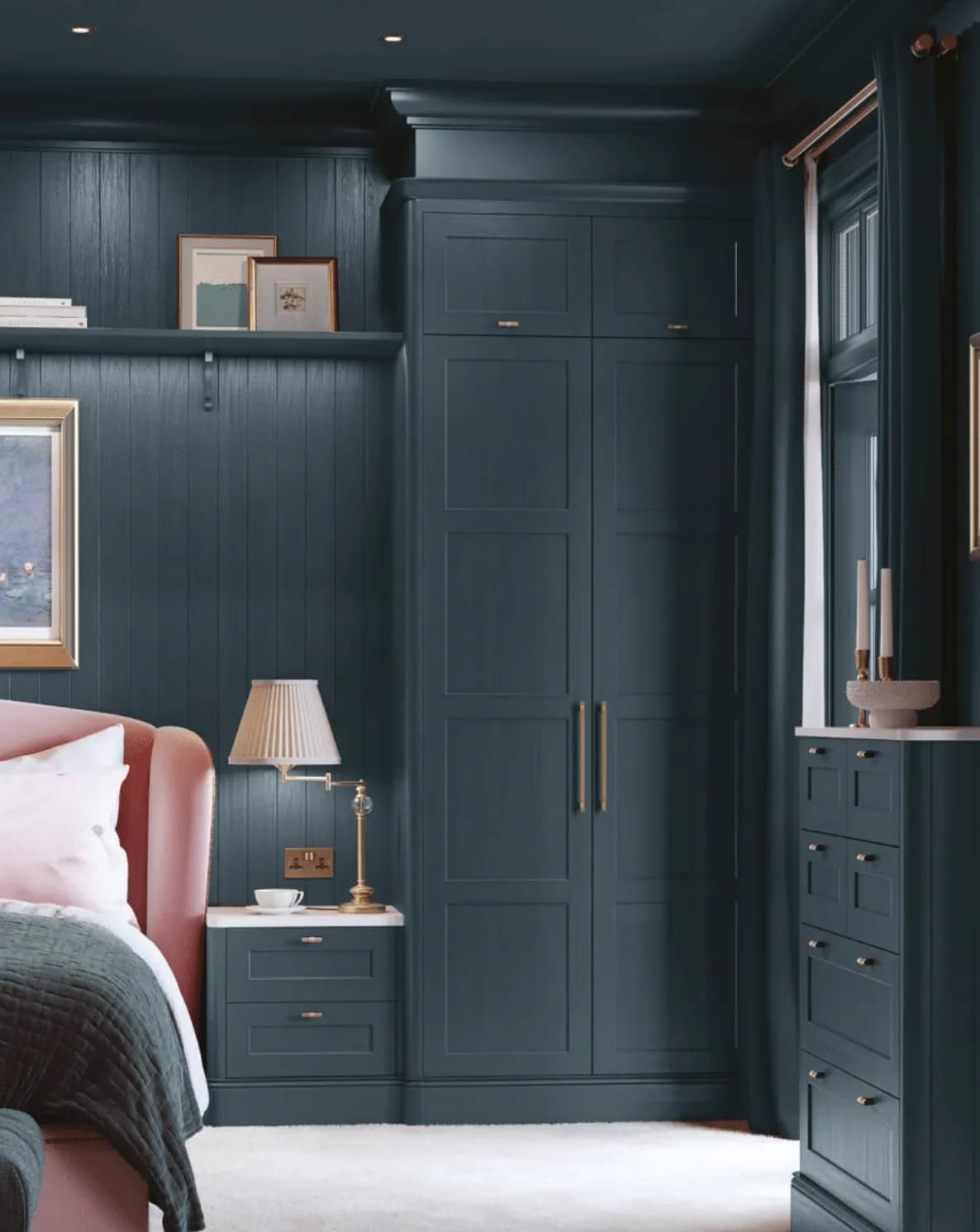 Dark teal fitted wardrobes and bedside drawers with slim brass handles, against panelled walls.