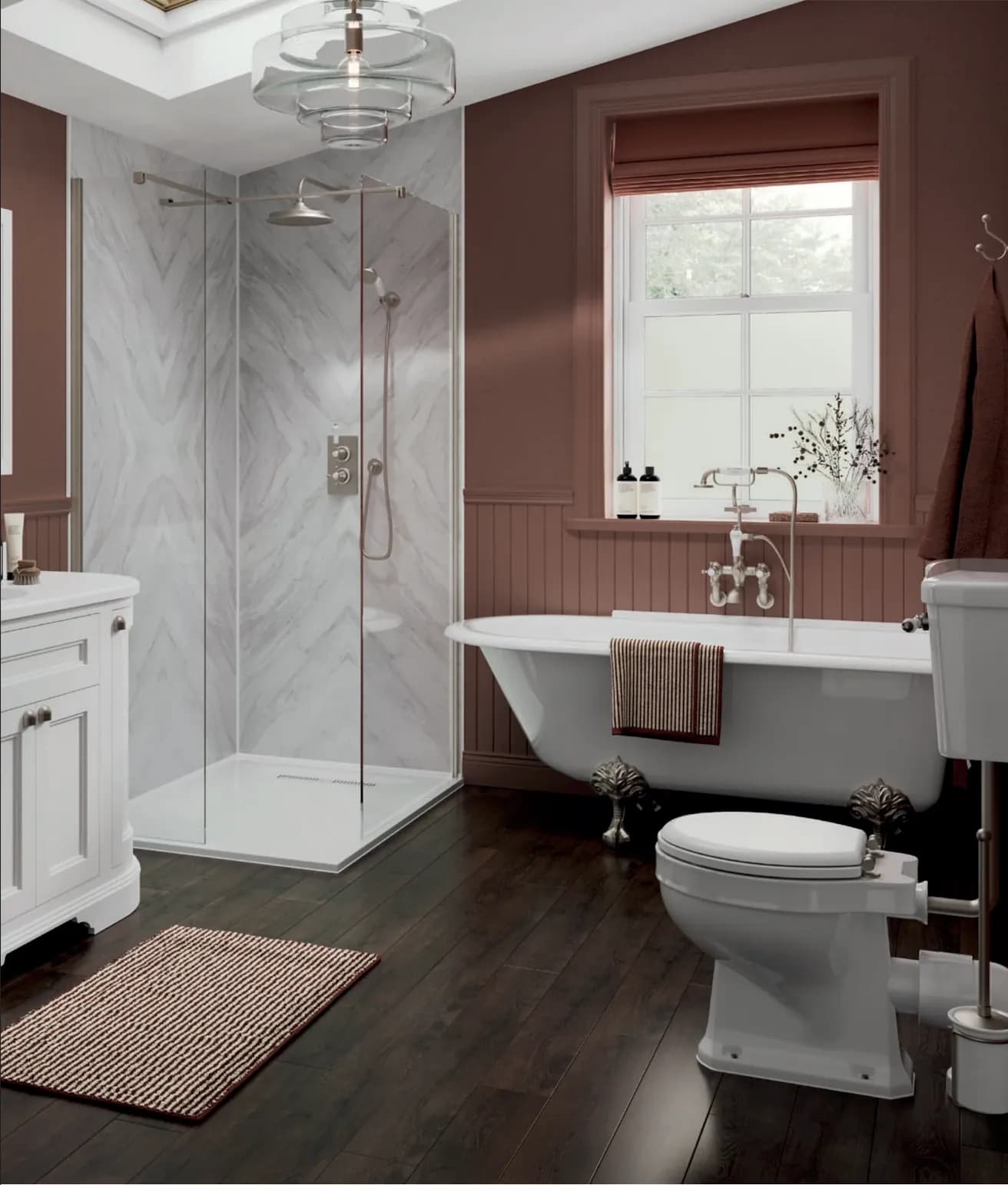 A claw-foot roll-top bath under a sash window in a clay-painted room, with a marble-panelled walk-in shower and a dark timber floor