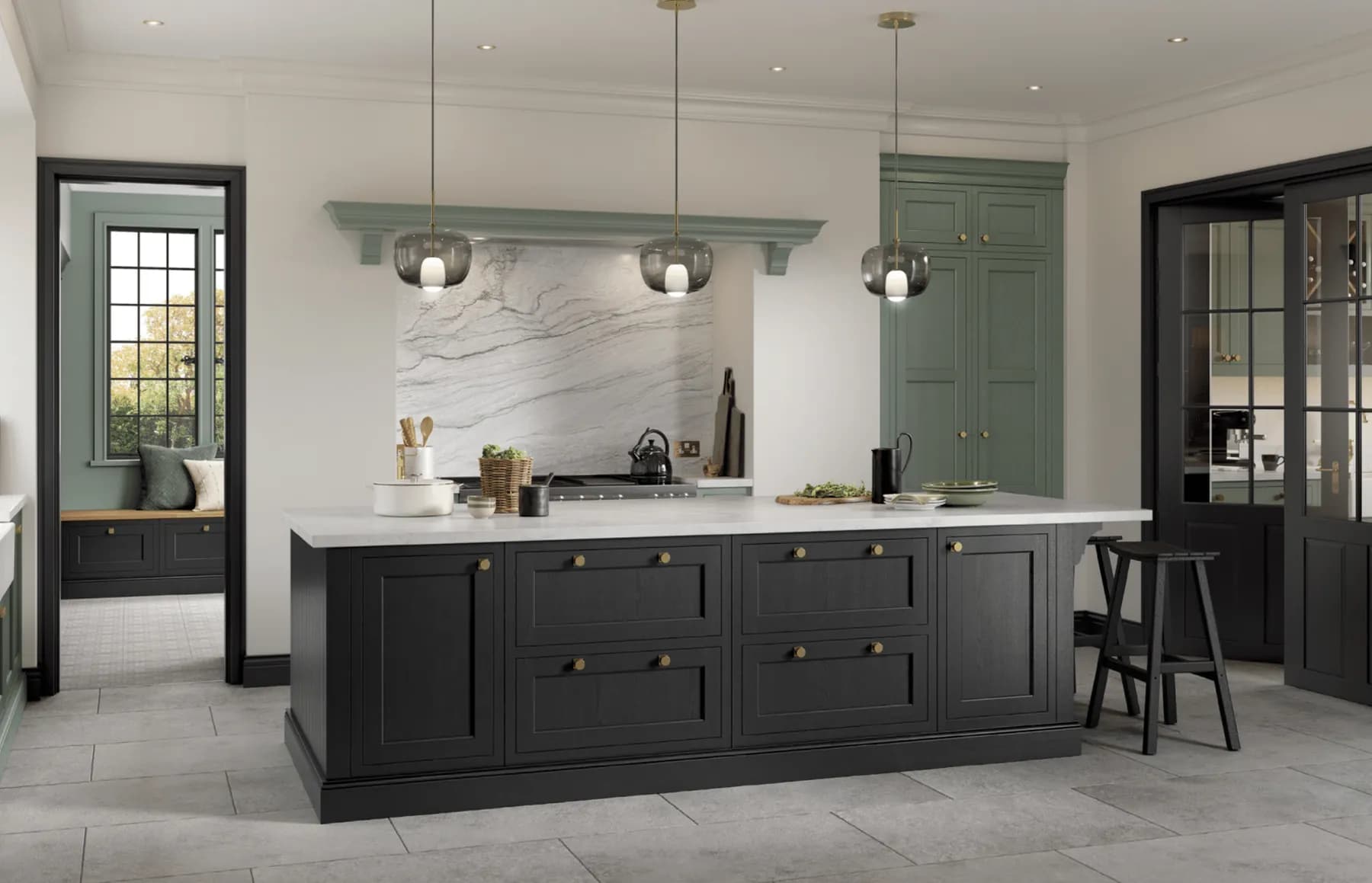 A near-black in-frame island with brass knobs and a pale worktop, sage green tall units beyond