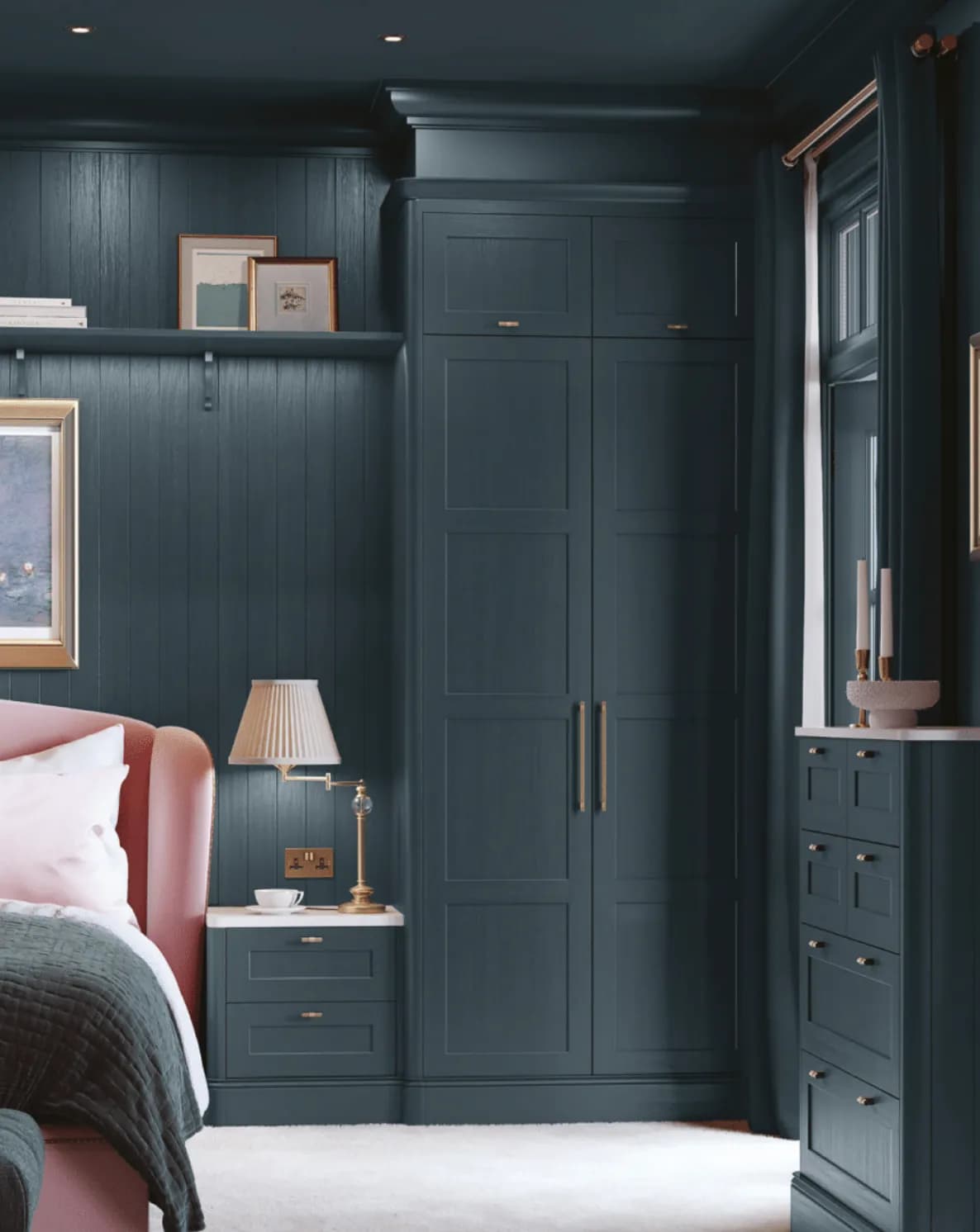 A full-height in-frame wardrobe painted deep teal with slim brass bar handles, beside a matching bedside drawer unit with a stone top