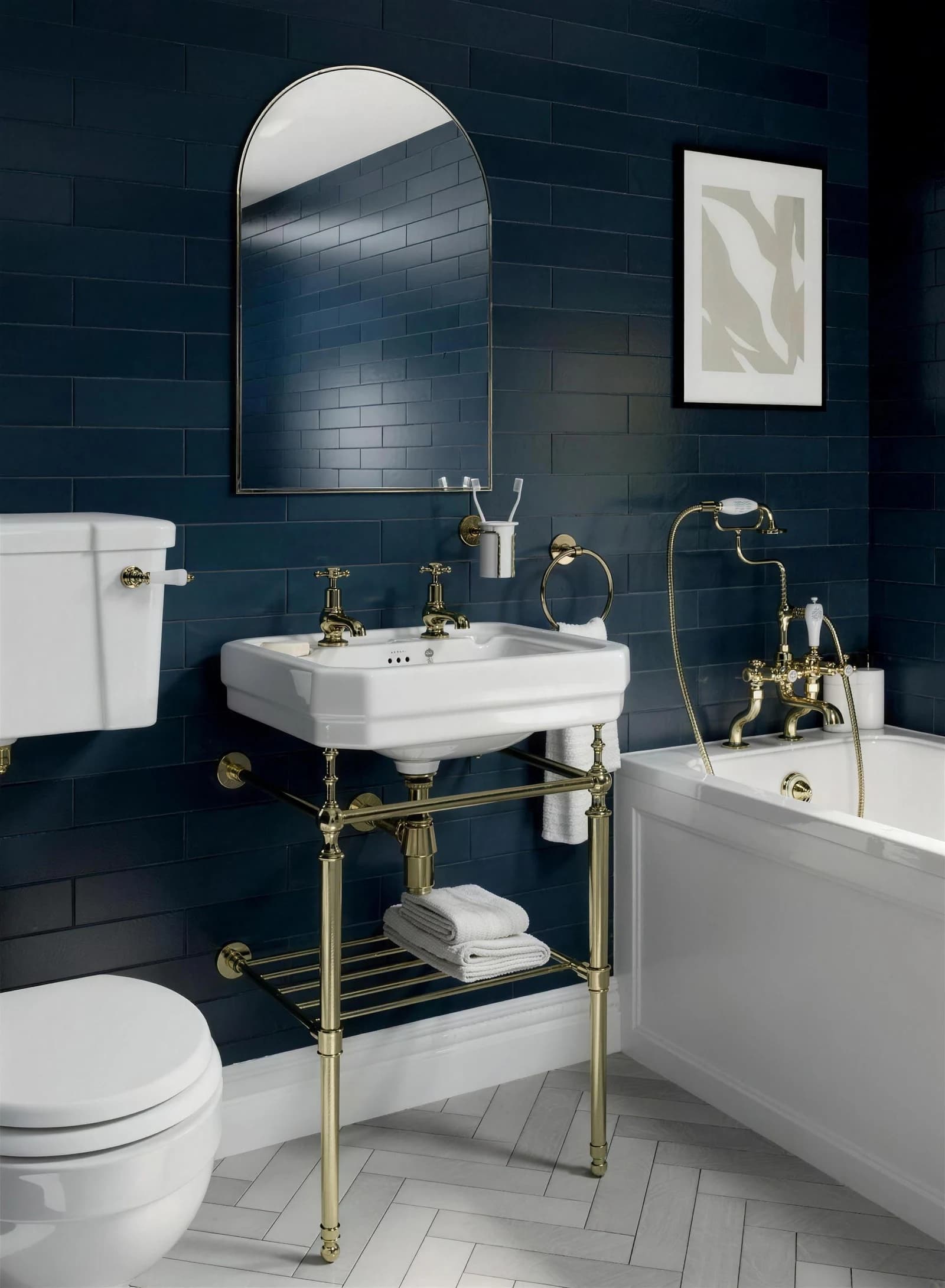 A compact bathroom tiled floor to ceiling in navy brick tile, with a washstand basin on a brass frame, an arched mirror, a close-coupled WC and a bath alongside