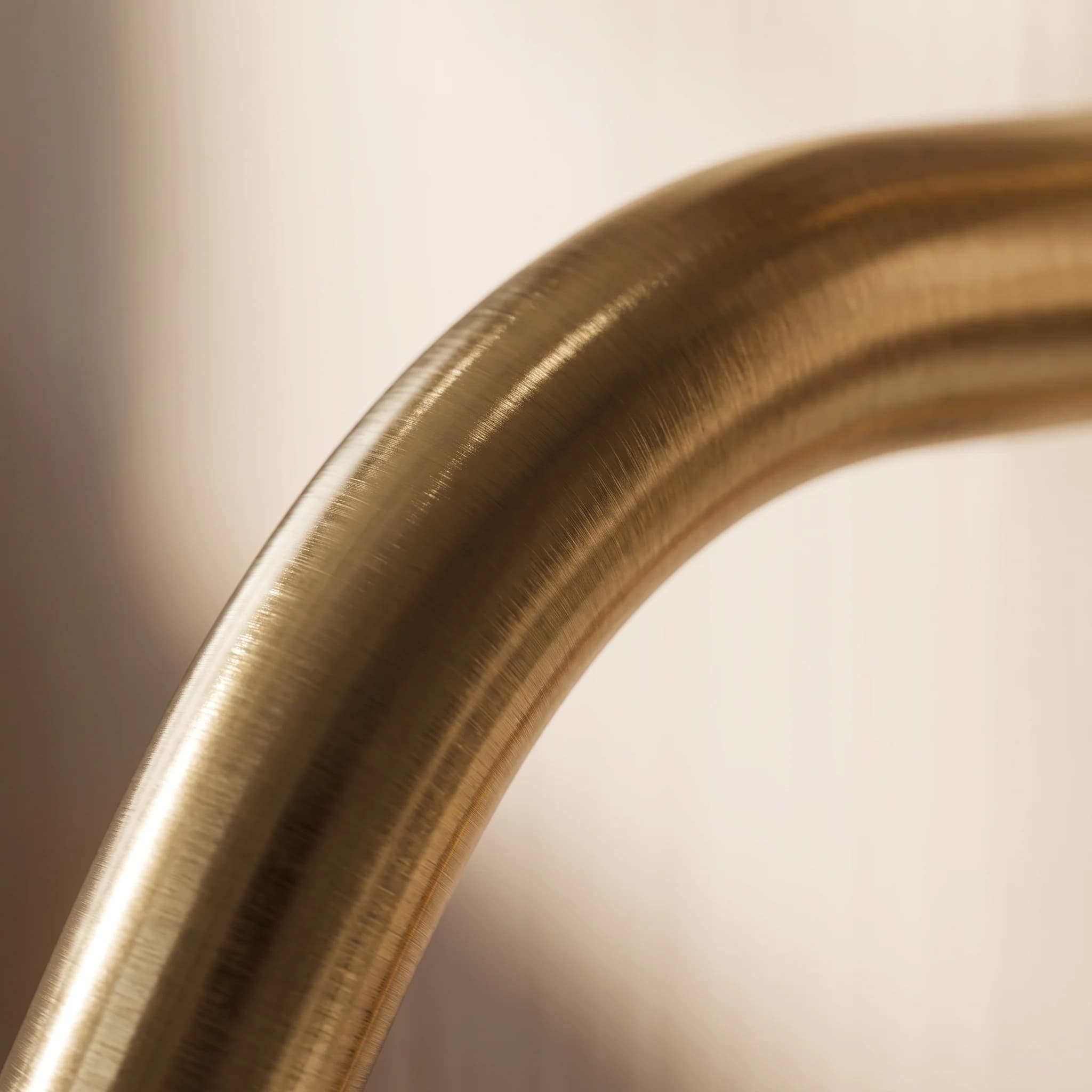 The arc of a brushed brass spout, close, against a pale wall — shown in brushed brass
