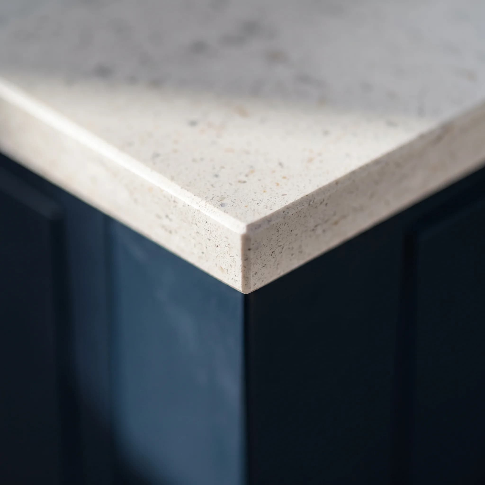 The mitred quartz edge of a worktop over a navy painted island