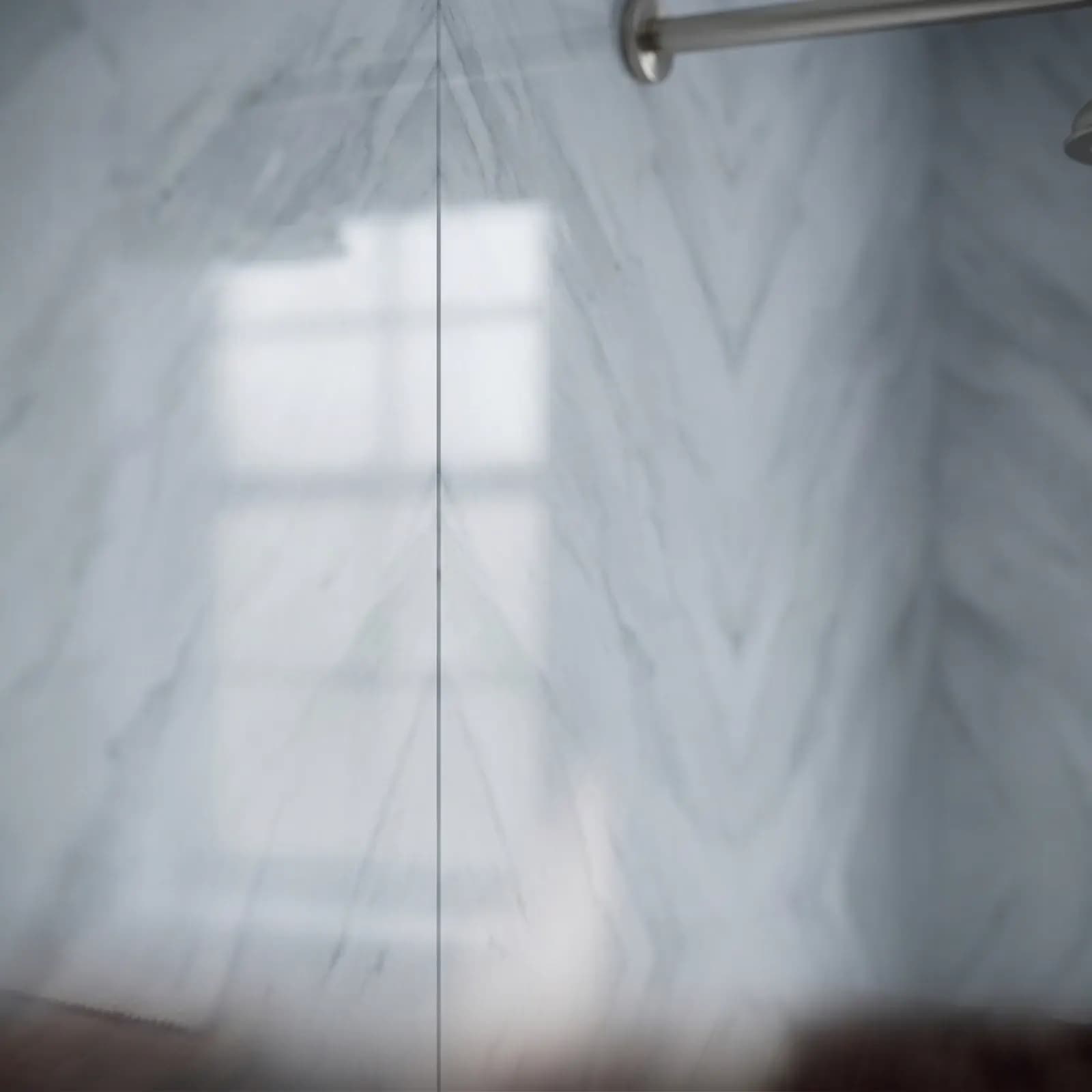 Book-matched veined stone panels behind a shower, a nickel rain head on the arm above